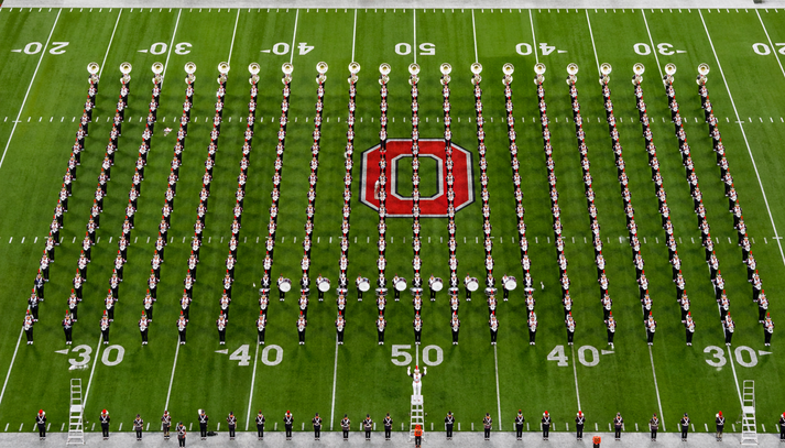 marching band lined up in perfect rows on a field, viewed from above, showing straight lines and spacing