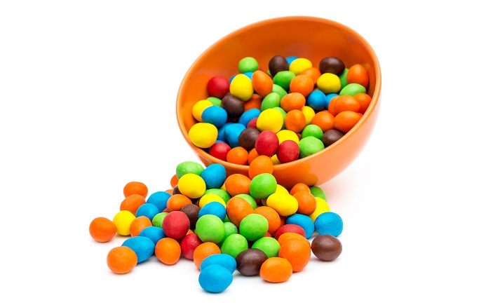 bowl of candies Sweet round candies scattered from bowl on white.