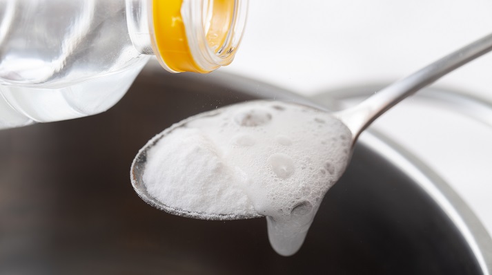 Foaming baking soda and vinegar Foaming baking soda slaked with vinegar in a spoon over a metal dish