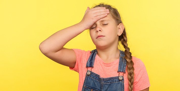 Portrait of forgetful sad little girl with braid in denim overalls gesturing facepalm with hand on forehead and expressing sorrow, blaming herself for bad memory.
