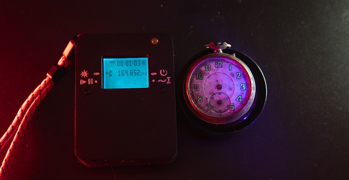 Dosimeter of radioactive radiation and old broken pocket watch with dangerous fluorescent paint. Violet light and green glow of numbers.