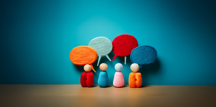 Colorful speech bubbles float above wooden figures. Group stands against a blue wall, suggesting communication and diverse thoughts.